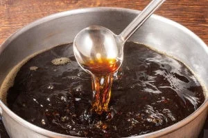 鍋の中の濃い色の鴨南蛮だしをお玉ですくう様子