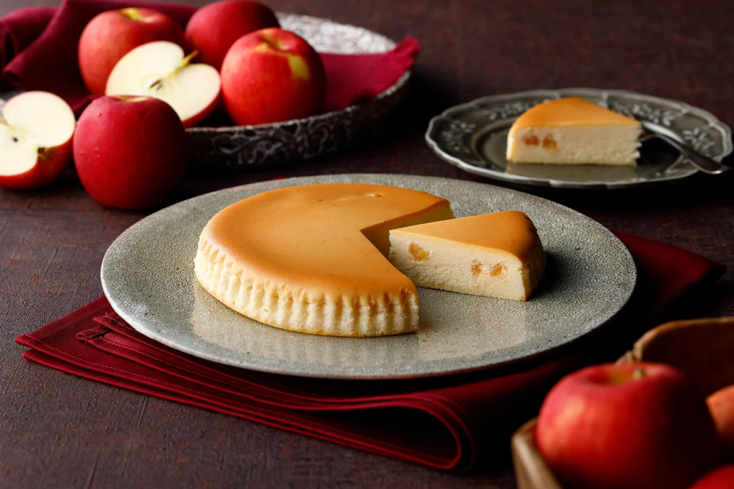 皿にのったカットされた御用邸アップルチーズケーキと周りのりんご