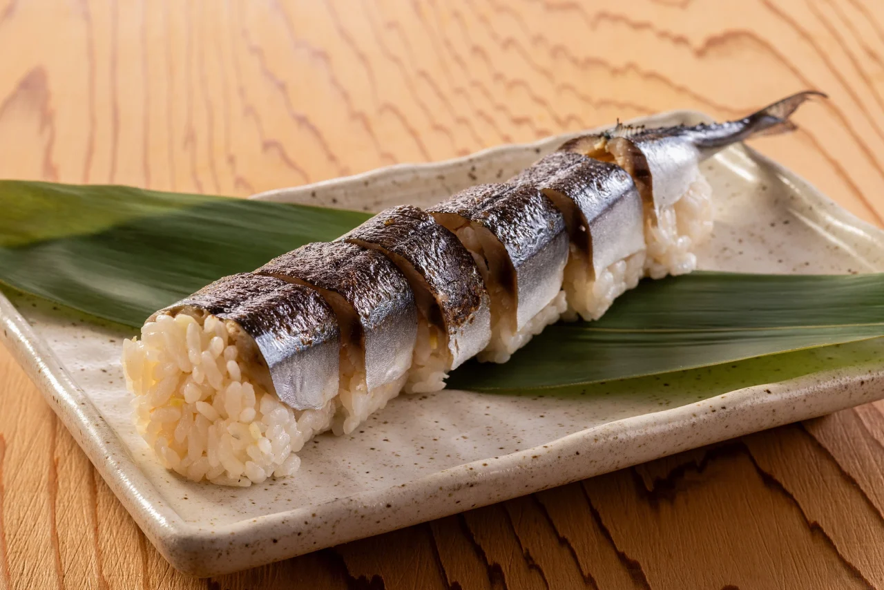 笹の葉と角皿に盛られたサンマ姿寿司。炙った皮目のサンマが酢飯に乗る