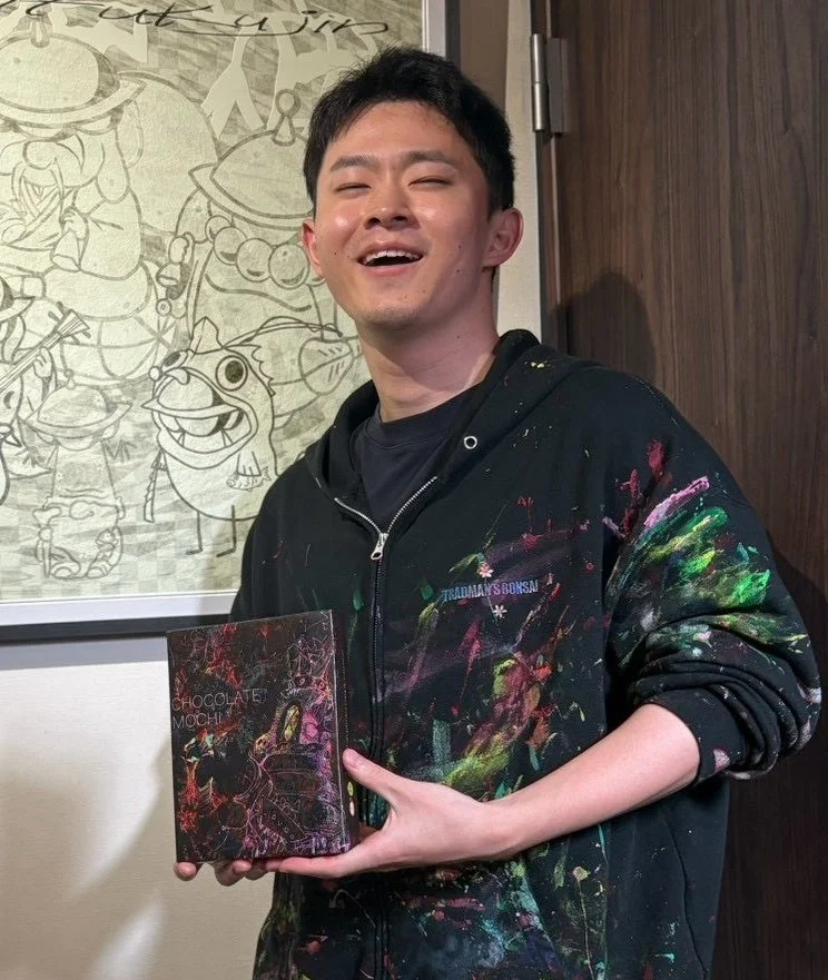 絵の具が飛び散ったパーカーの男性がきびだんごのパッケージを持つ様子