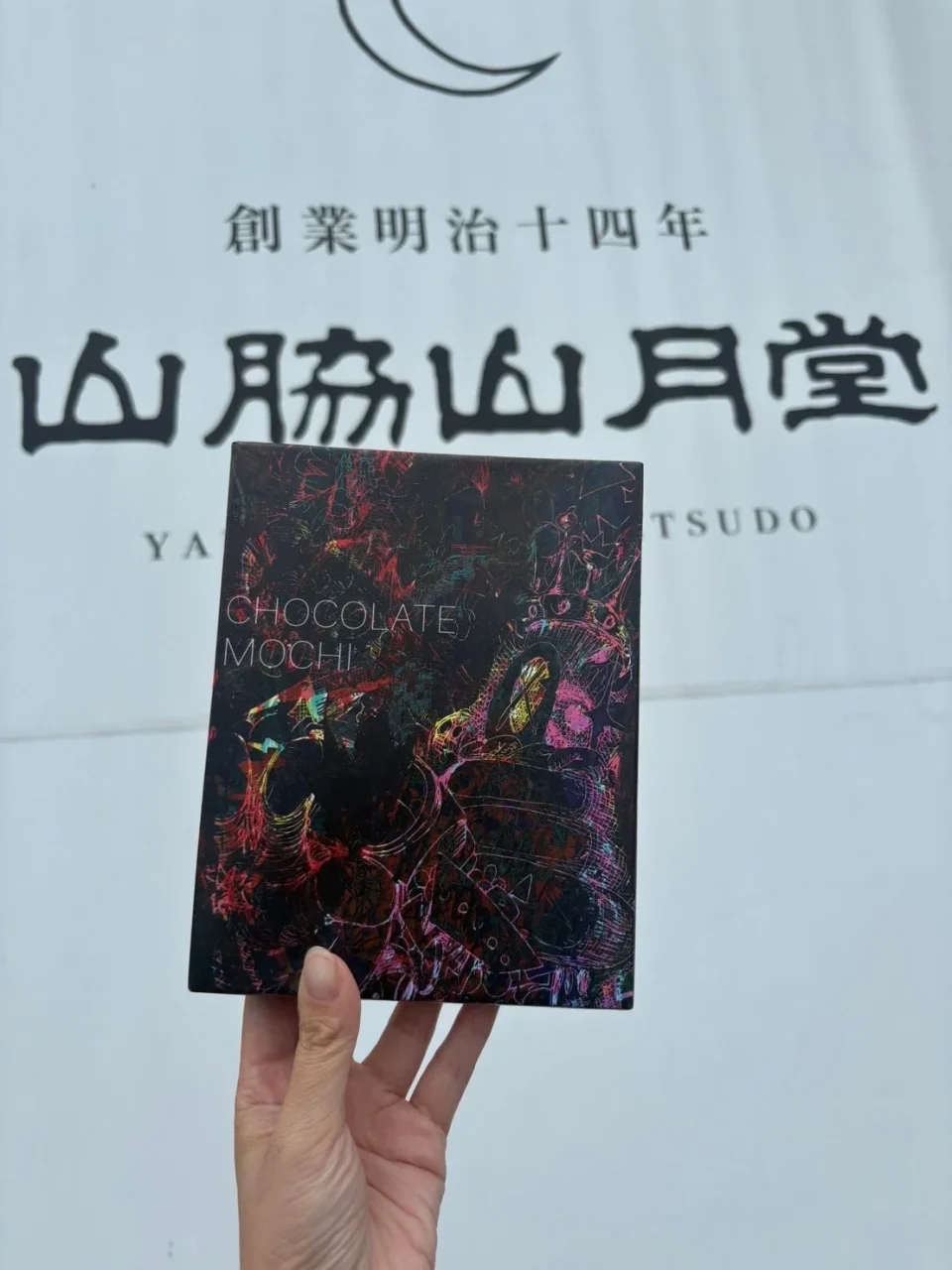 ちょこきびだんごのパッケージを手に持つ様子。黒地にカラフルなアート