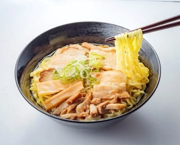 喜多方チャーシューメン。黒い丼に豚バラチャーシューとメンマ、ねぎを盛り、箸で麺を持ち上げた様子