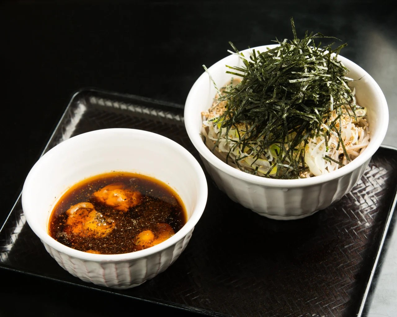 刻み海苔をのせた蕎麦の器と、つけ汁の器が黒いトレーに並ぶ様子