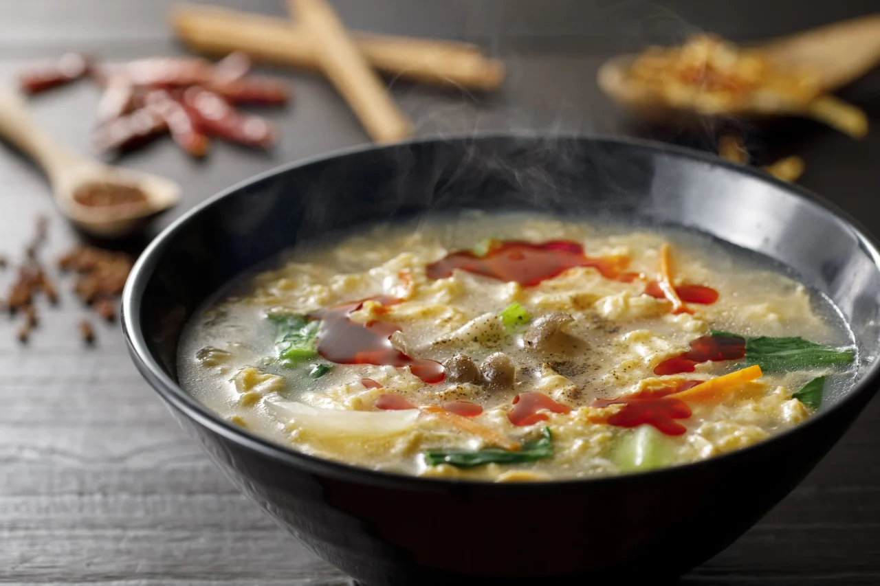 黒い丼に入った酸辣湯麺。紅油がかかった玉子のとろみスープから湯気が立つ