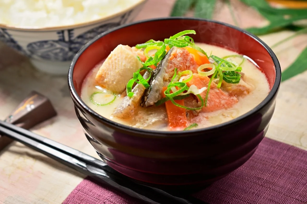 赤い椀に入ったかす汁。ねぎや野菜、魚の具材が入り湯気が立つ