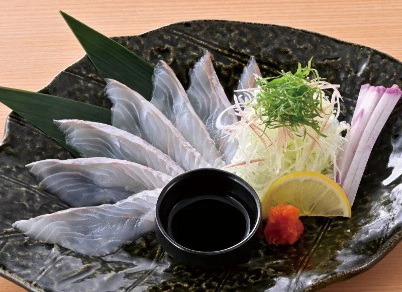 ヒラメの薄造り。黒い皿に薄切りの刺身、薬味、レモン、小皿のたれ