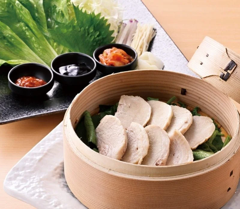 ポッサム風豚の蒸籠蒸し。蒸籠に薄切り肉が並び、薬味と小皿が添えられている