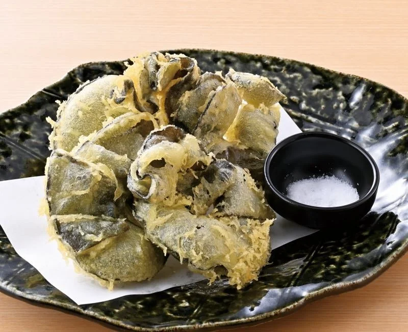 黒い皿に盛られた、塩を添えためかぶの天ぷら