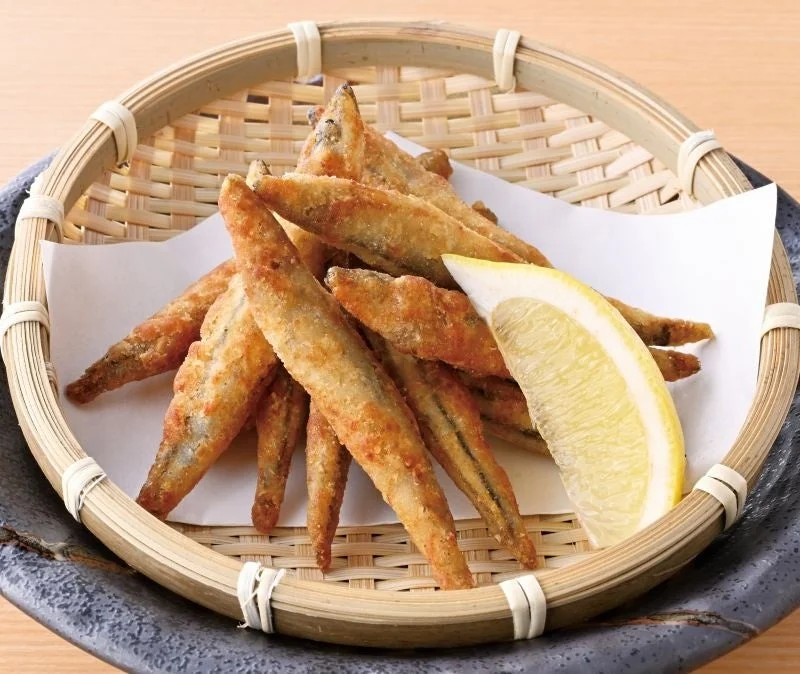 きびなごの唐揚げ。竹ざるに敷いた紙に盛り、レモンを添えた様子