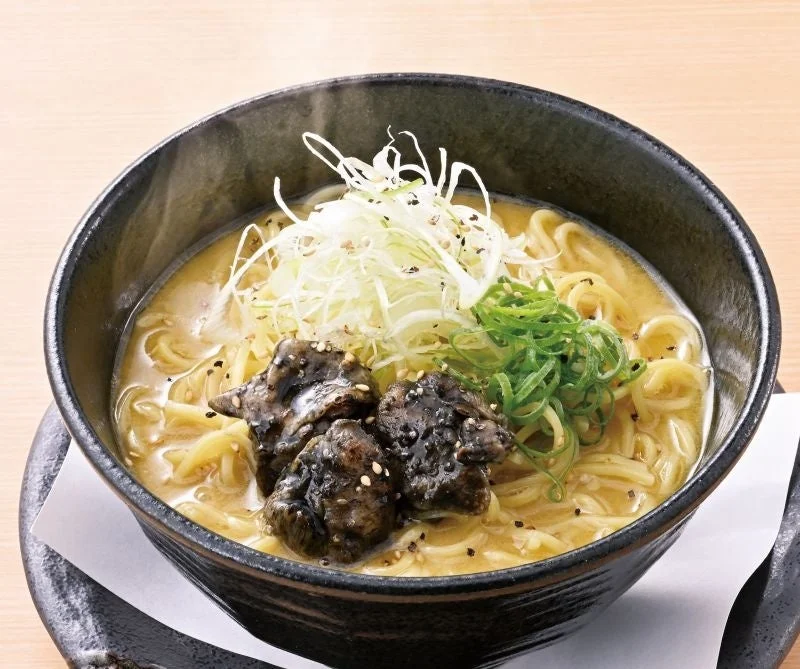 炭火香る鶏白湯ラーメン。黒い丼に白ネギと青ネギをのせた麺