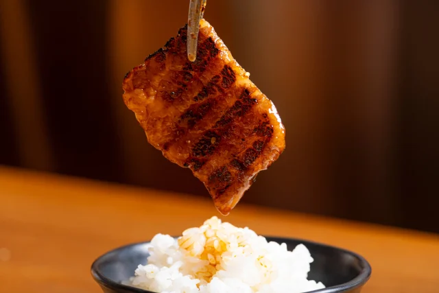 たれ焼肉のんきの焼いた肉を箸で持ち上げ、白米の上に運ぶ様子