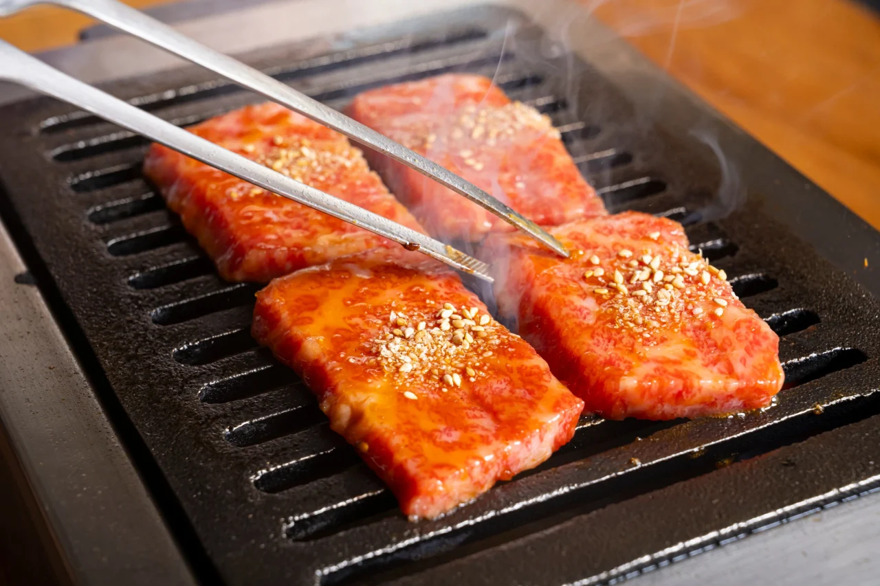 ロースターの網でトングで焼かれるたれ漬けの焼肉