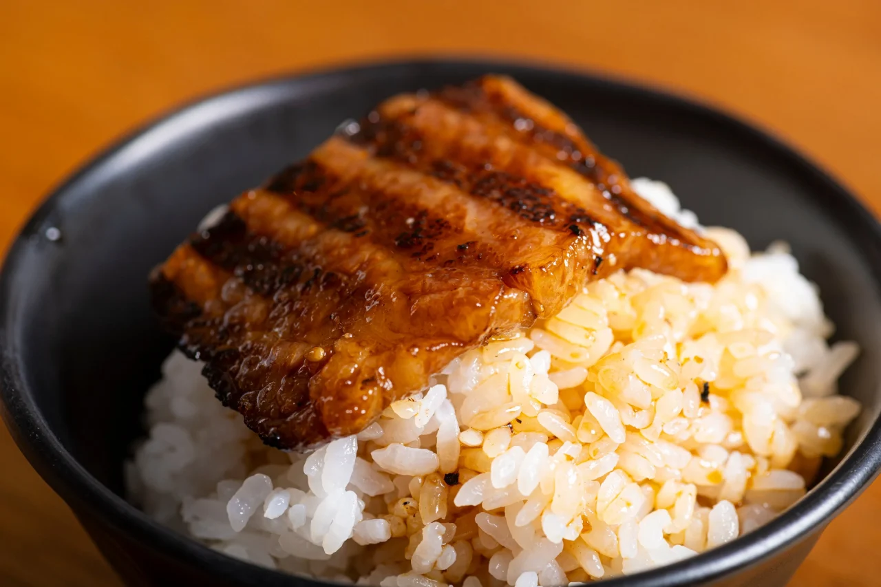 釜で炊いた熱々のご飯の上にたれ焼きの肉をのせた黒い丼