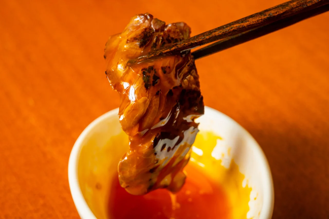 箸でつまんだ焼肉を小皿のたれにつけている様子