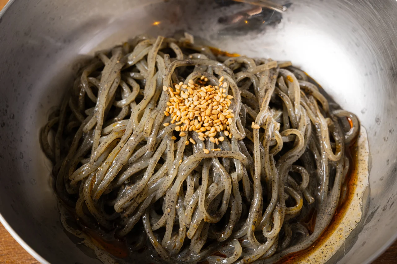 汁なし黒ごま坦々冷麺。ごまをのせた黒っぽい麺が金属の器に盛られている