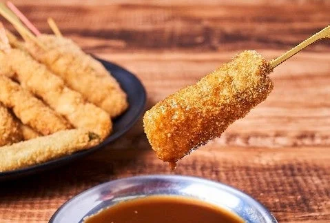 串カツ田中の串カツ。衣をまとった串を持ち上げ、手前にソース