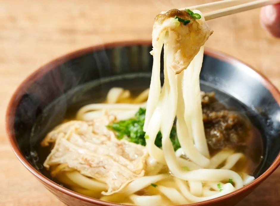 田中のかすうどん。黒い器のお出汁に入ったうどんを箸で持ち上げた様子