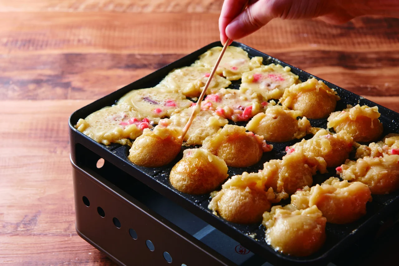 たこ焼き器で焼く途中のたこ焼きを竹串で返している様子