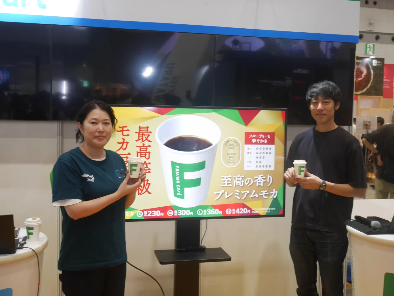SCAJ2026ブースで「プレミアムモカ」のカップを持つ男女とモニター