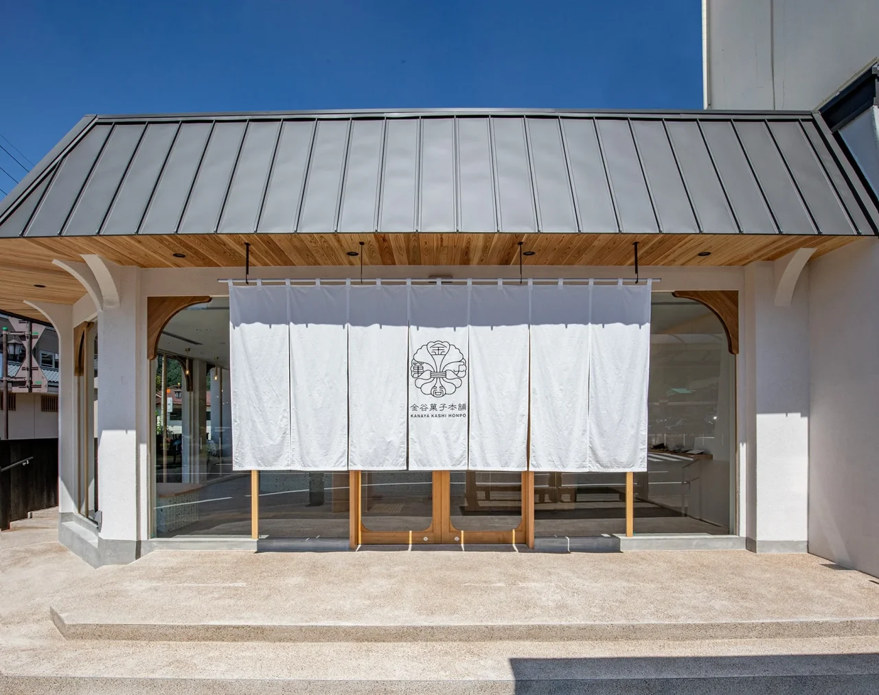 金谷菓子本舗 鬼怒川温泉駅前店の外観。白い暖簾と金属屋根