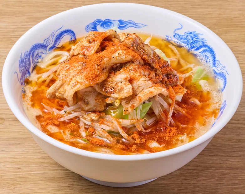 豚しゃぶ辛ラーメン。青い龍柄の丼に豚しゃぶともやしを盛り、赤い辛味粉をかけた一杯