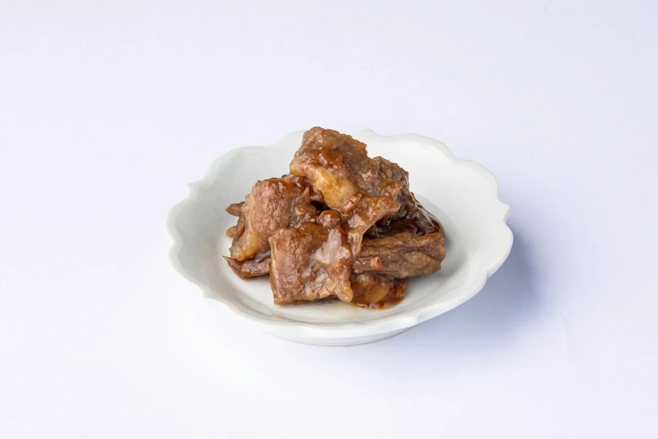 白い花形の小皿に盛られた、煮込んだ牛肉コウネの焼肉
