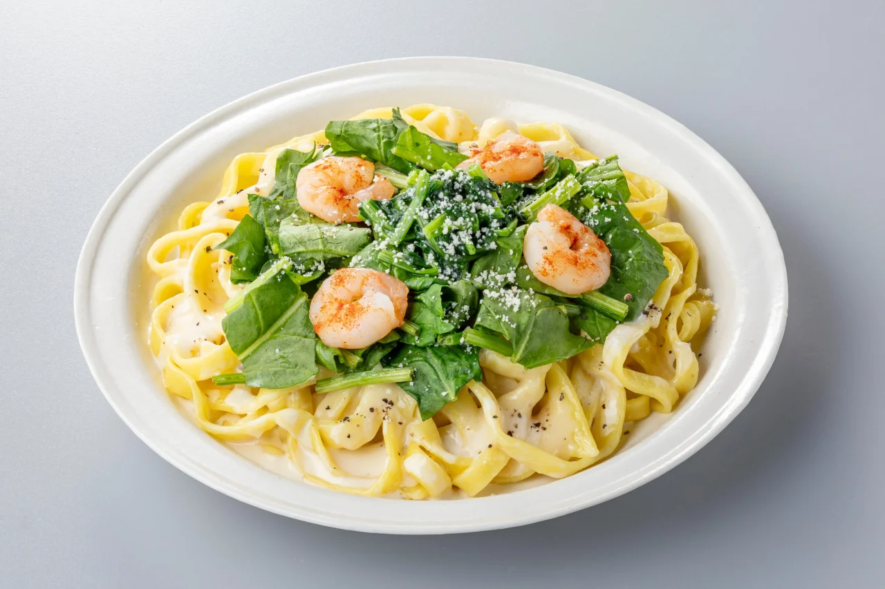 白い皿に盛られたクリームソースの平打ち麺、ほうれん草とエビ添え