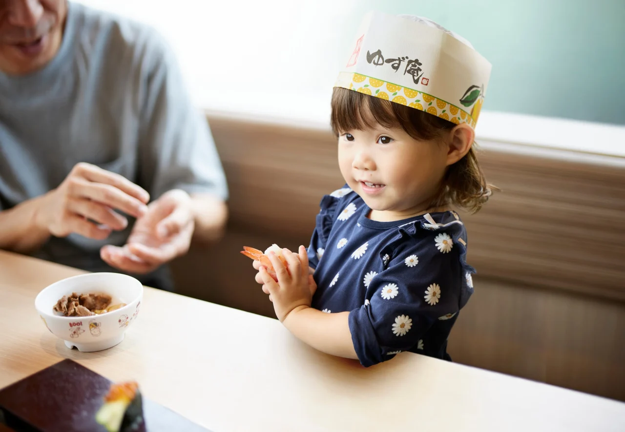 ゆず庵のオリジナル和帽子をかぶり、エビの寿司を手にする女の子