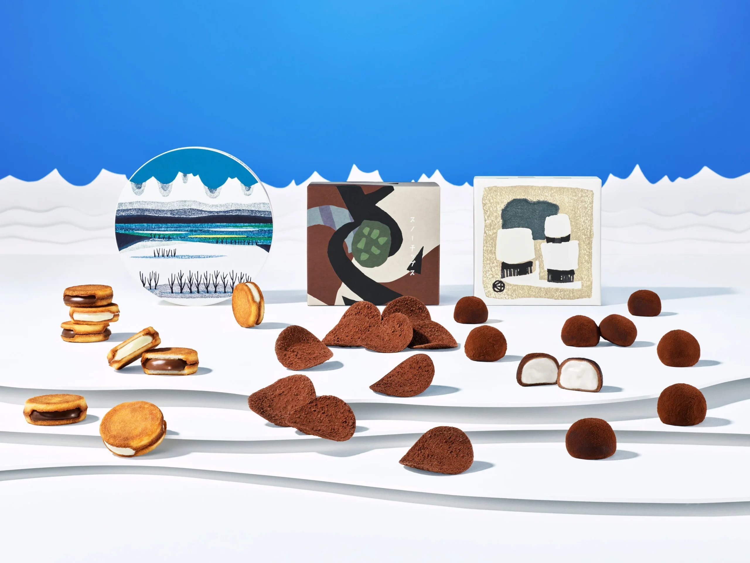 SNOWSのお菓子と版画パッケージを雪景色に並べた告知ビジュアル