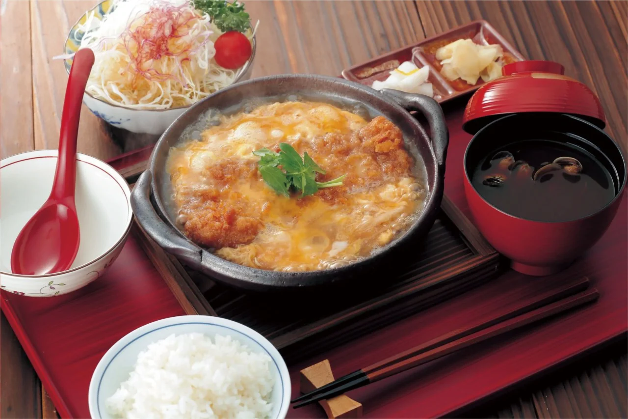 和豚かつ煮御前。卵とじのかつ煮の鍋にご飯、しじみ味噌汁、サラダが並ぶ
