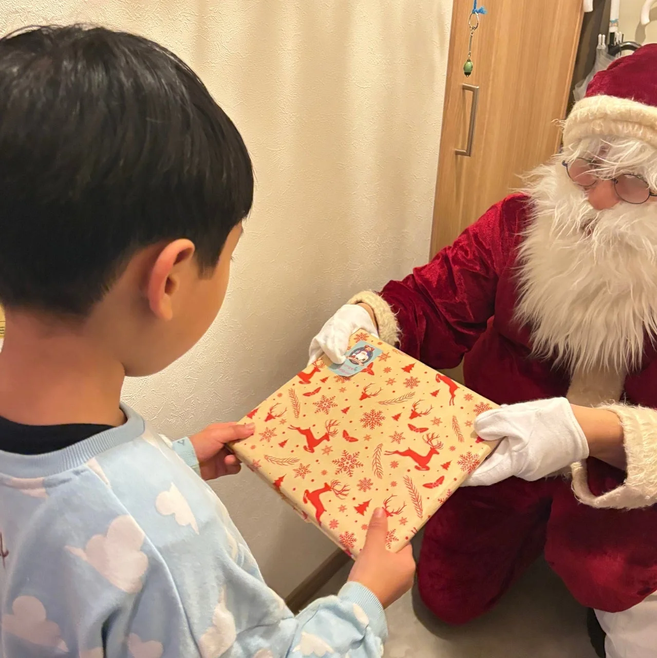 サンタクロース姿の人が男の子にクリスマス柄の包みを手渡す様子