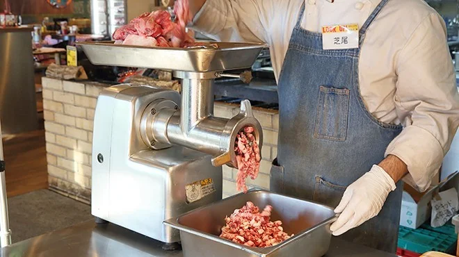 12.5mm超荒びきハンバーグ用の肉をミンサーで挽く調理スタッフ