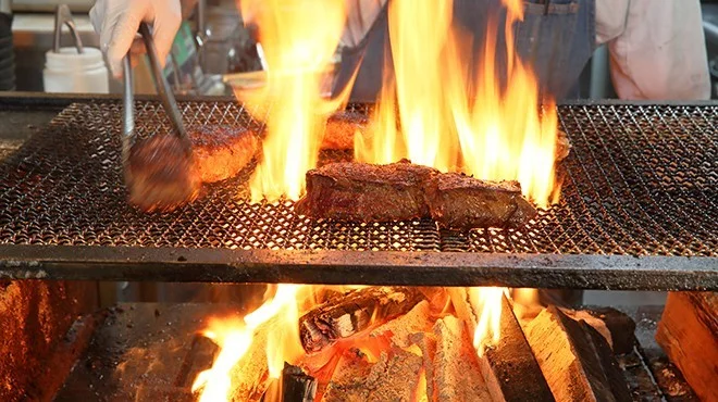 「炭と薪」の二刀流焼き。炎が上がる網の上で肉を焼く様子