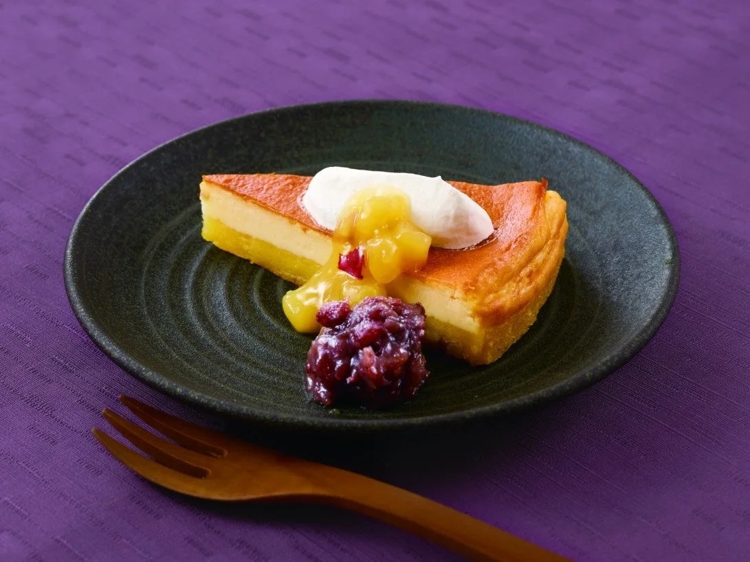 お芋のチーズケーキ。ホイップとお芋ソース、小豆が添えられた黒い皿の一切れ