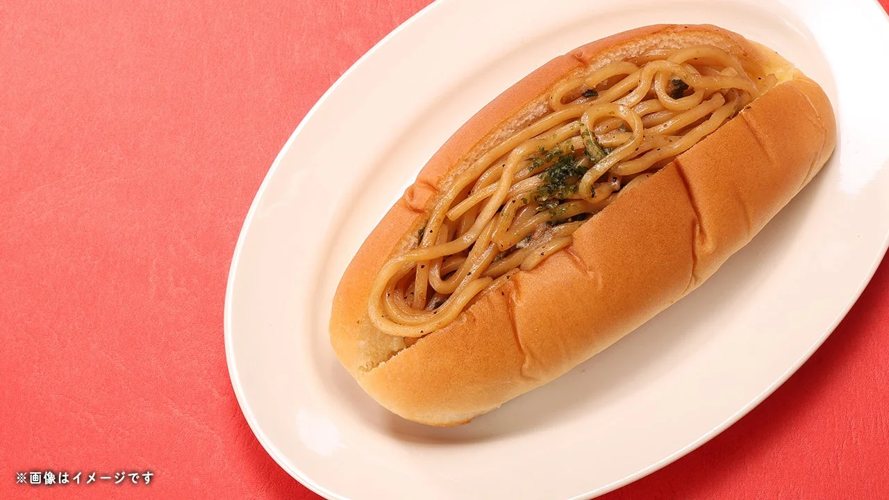 油そばパン。ロールパンに油そば風の麺とネギを挟み白い皿に載せた様子