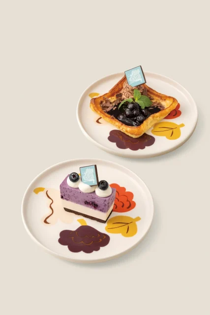 ブルーベリーのケーキとパンケーキ風デザートが並ぶ、ロゴチョコ付き2枚の皿