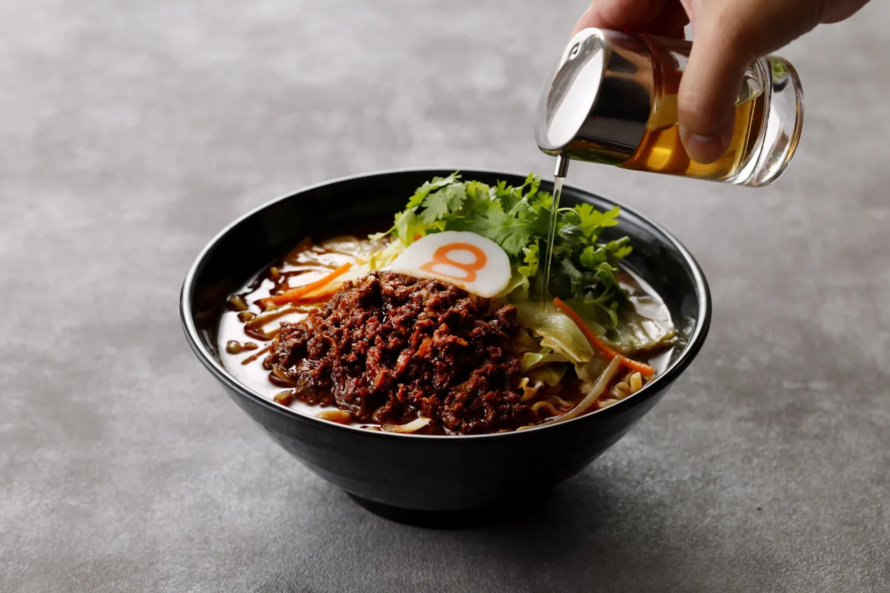 辣醤にパクチーをのせたラーメンに、８番酢を回しかける様子