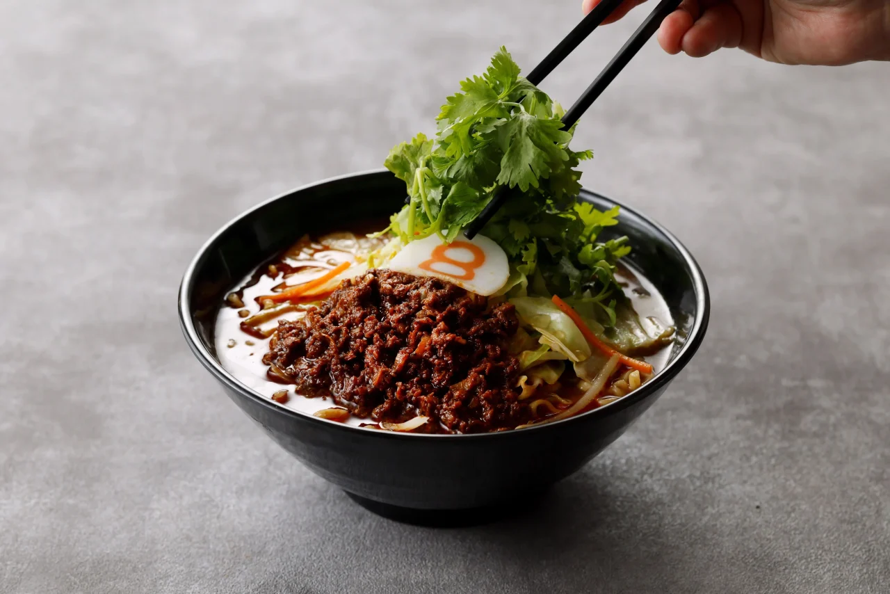 パクチー増しを箸でのせる、肉味噌と野菜入りのラーメン